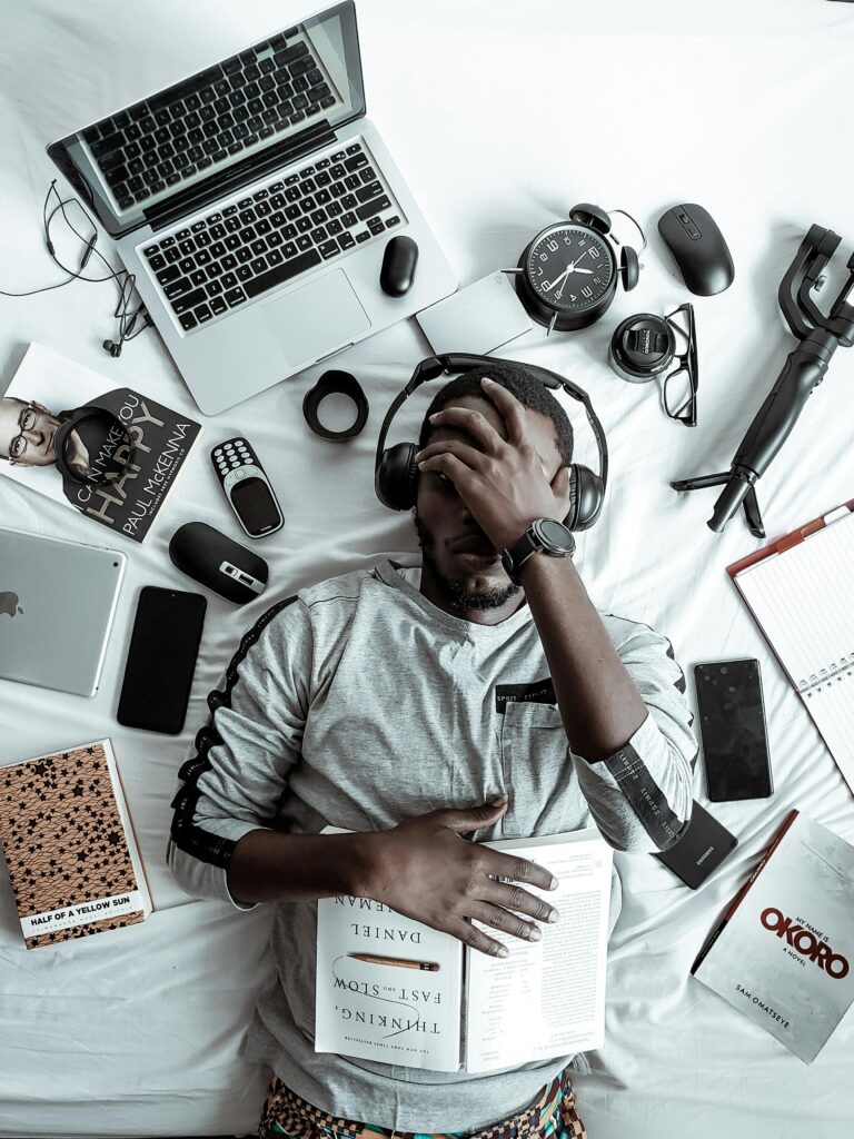À propos A young man lying on a bed surrounded by modern gadgets, books, and tech devices, illustrating digital lifestyle.